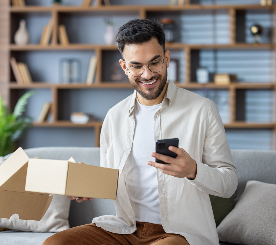 Person öffnet Paket nach Online-Bestellung und nutzt Smartphone